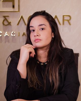 Dra. Yvina Monteiro, sentada à mesa do escritório, com o logo da Monteiro & Aguiar ao fundo
